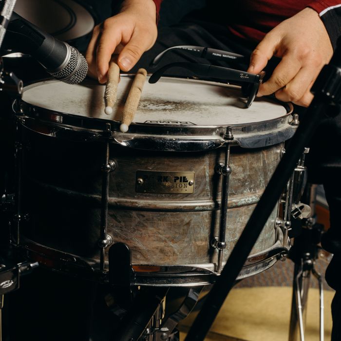 Close-up shot of a drummer playing a snare drum with drumsticks in a music studio.