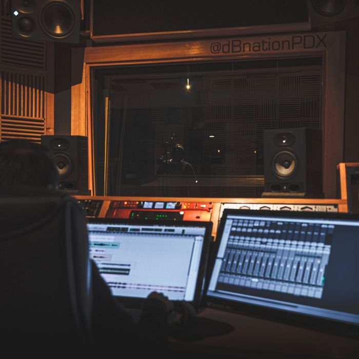 Back view of crop anonymous sound man creating musical arrangement for song while working on desktop computers with track on screen in recording studio